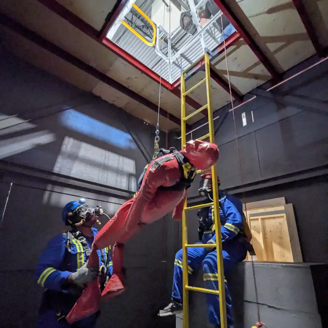 Rescue team performing confined space rescue with tripod, harness, and breathing apparatus